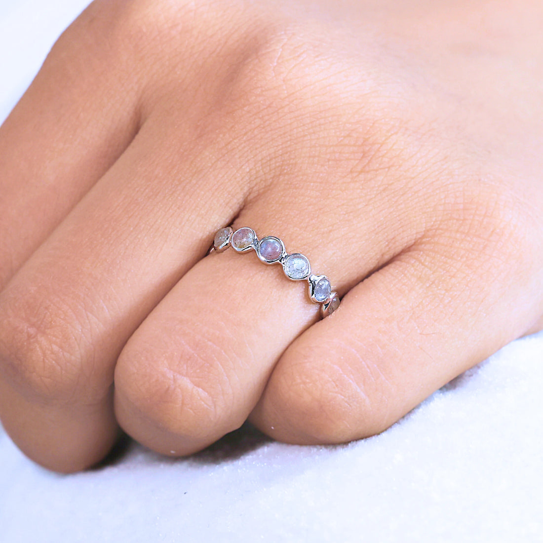 Angled close up shot of a sterling silver labradorite ring on an off-white velvet background with round iridescent stones