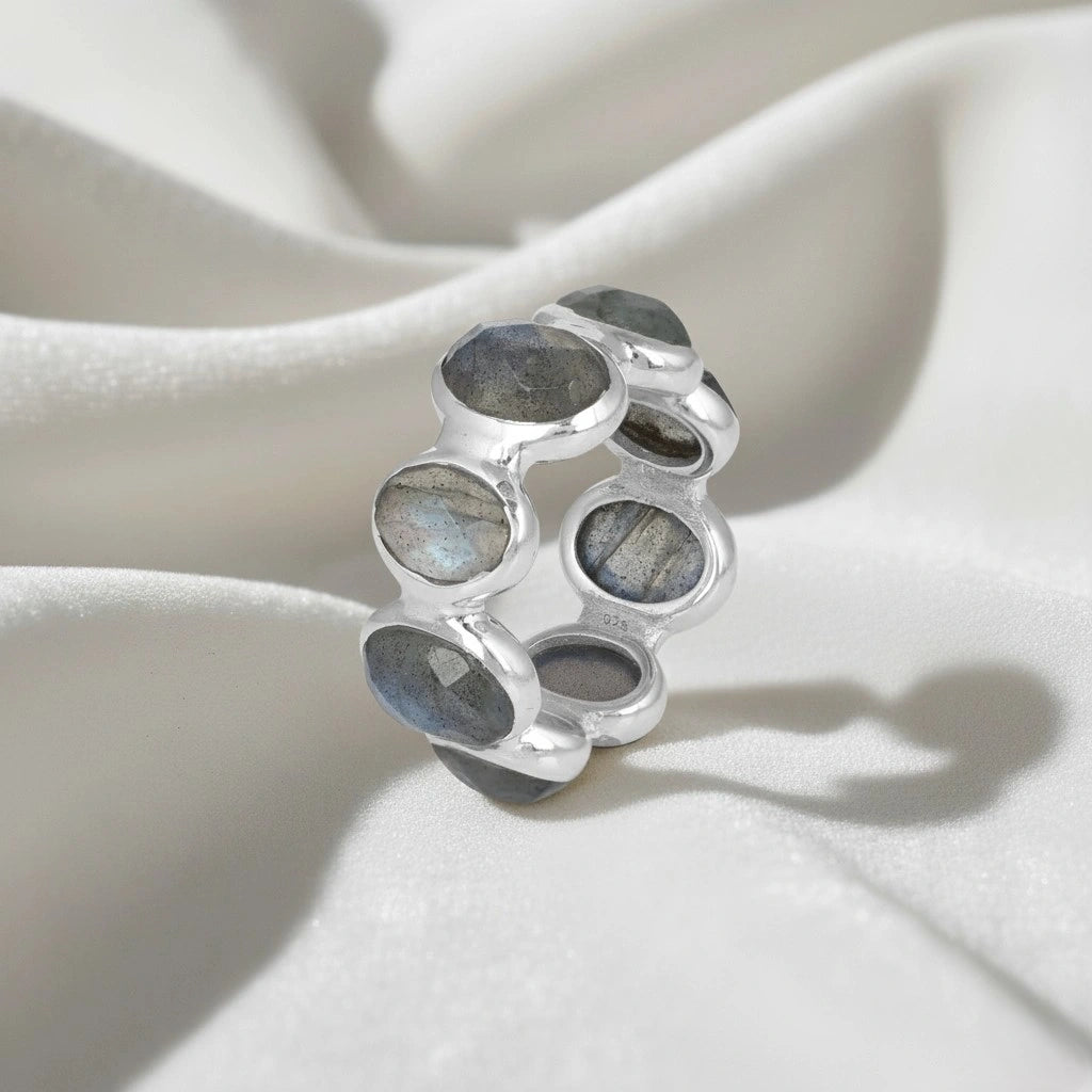 Silver labradorite ring with seven oval iridescent gray blue gemstones in the chunky setting shown at a slight angle on a white velvet.