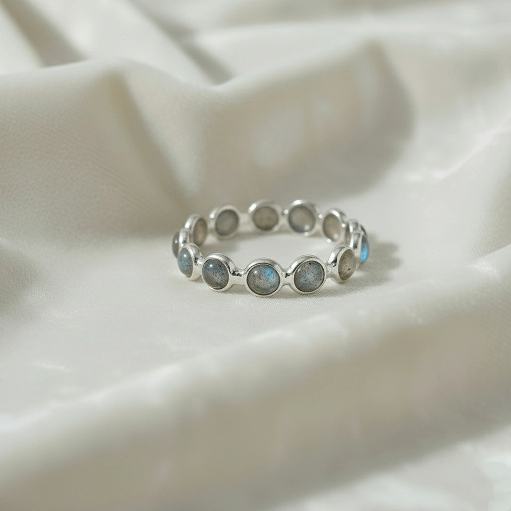 Horizontal close up shot of a sterling silver labradorite ring on a white velvet background with round iridescent stones