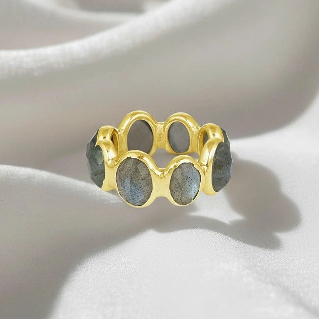 Silver labradorite ring with a gold vermeil band and oval iridescent gray blue gemstones shown at a slight angle on a white velvet fabric.