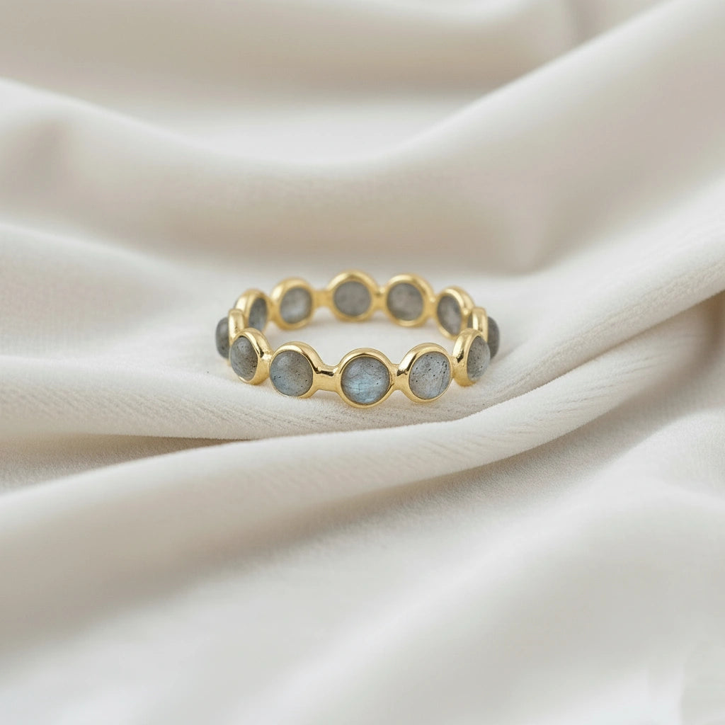 Horizontal close up shot of a gold-plated sterling silver labradorite ring on a white velvet background with round stones