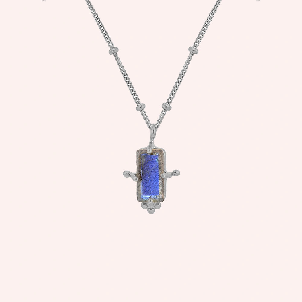 Gemstone_necklace_in_sterling_silver_with_a_baguette_labradorite_stone_at_front_angle_view_on_solid_pink_background