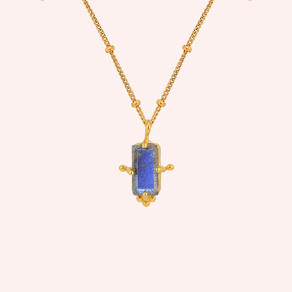 Gemstone_necklace_in_gold_plated_silver_with_a_baguette_labradorite_stone_at_front_angle_view_on_solid_pink_background