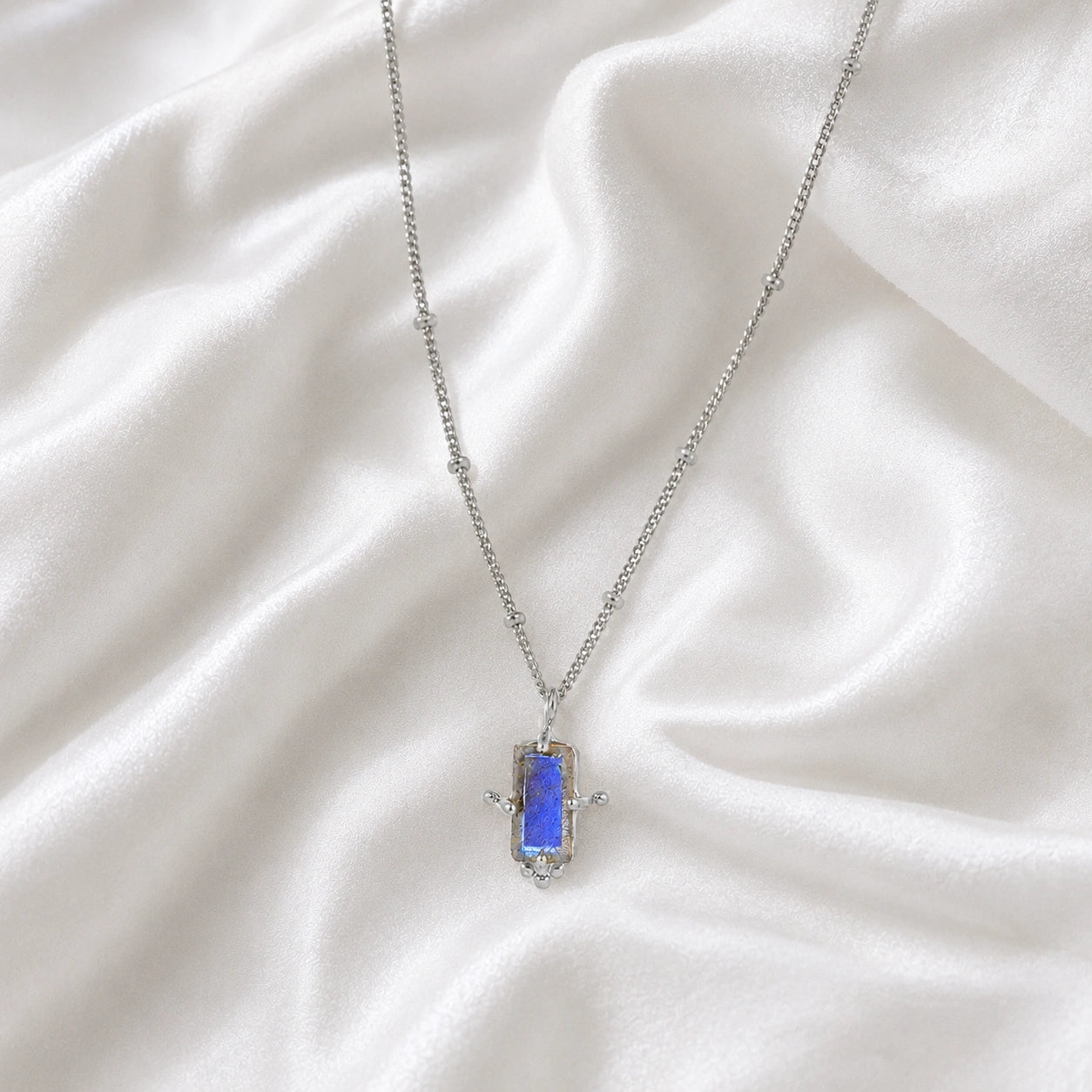 Gemstone_necklace_in_sterling_silver_with_a_baguette_labradorite_stone_at_front_angle_view_on_soft_fabric_background