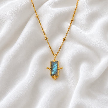 Gemstone_necklace_in_gold_plated_silver_with_a_baguette_labradorite_stone_at_front_angle_view_on_soft_fabric_background
