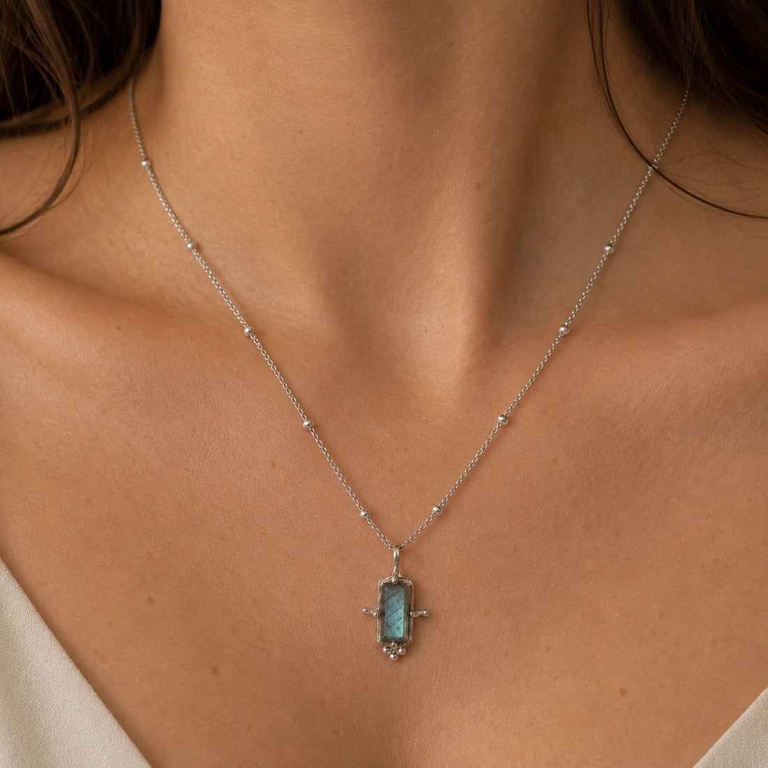 Gemstone_necklace_in_gold_plated_silver_with_a_baguette_labradorite_stone_at_front_angle_view_on_soft_fabric_background
