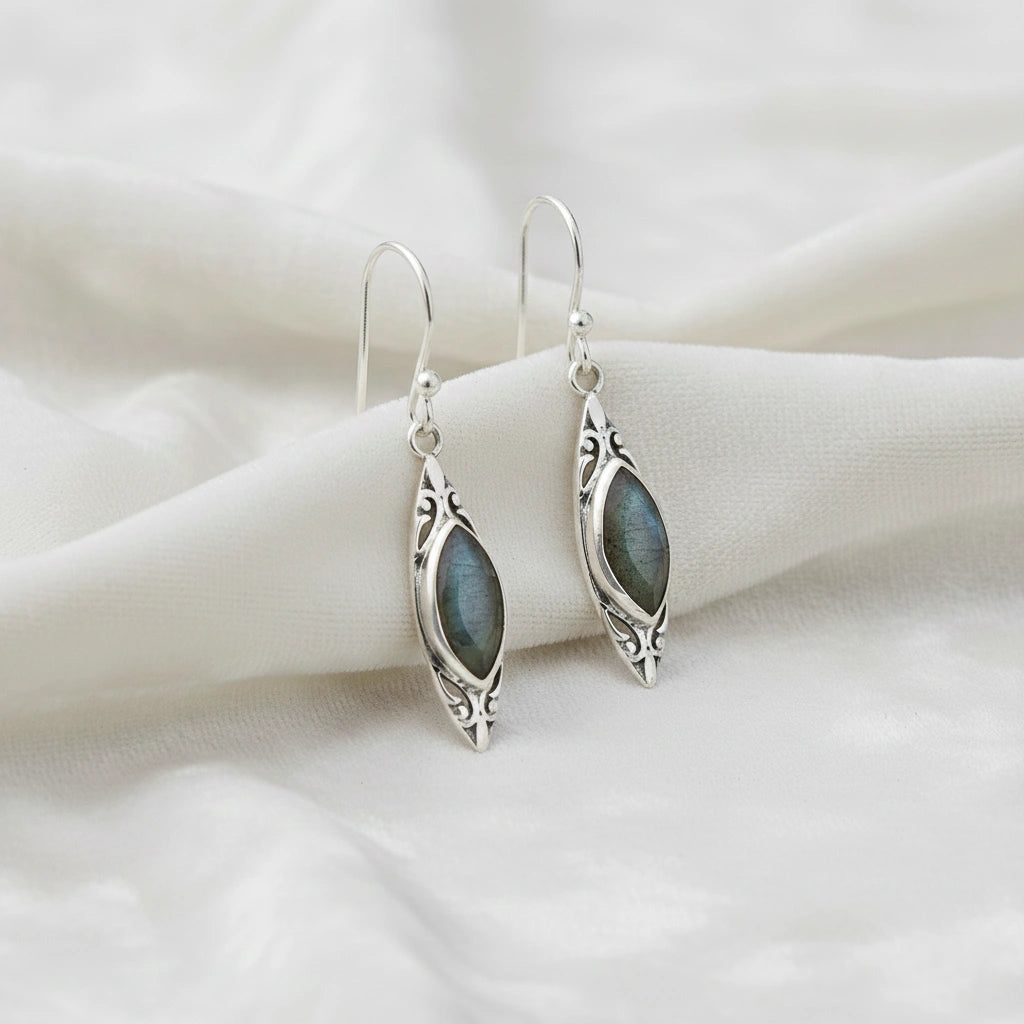 Marquise earrings silver dangle design with a decorative border and central labradorite viewed straight on soft white fabric