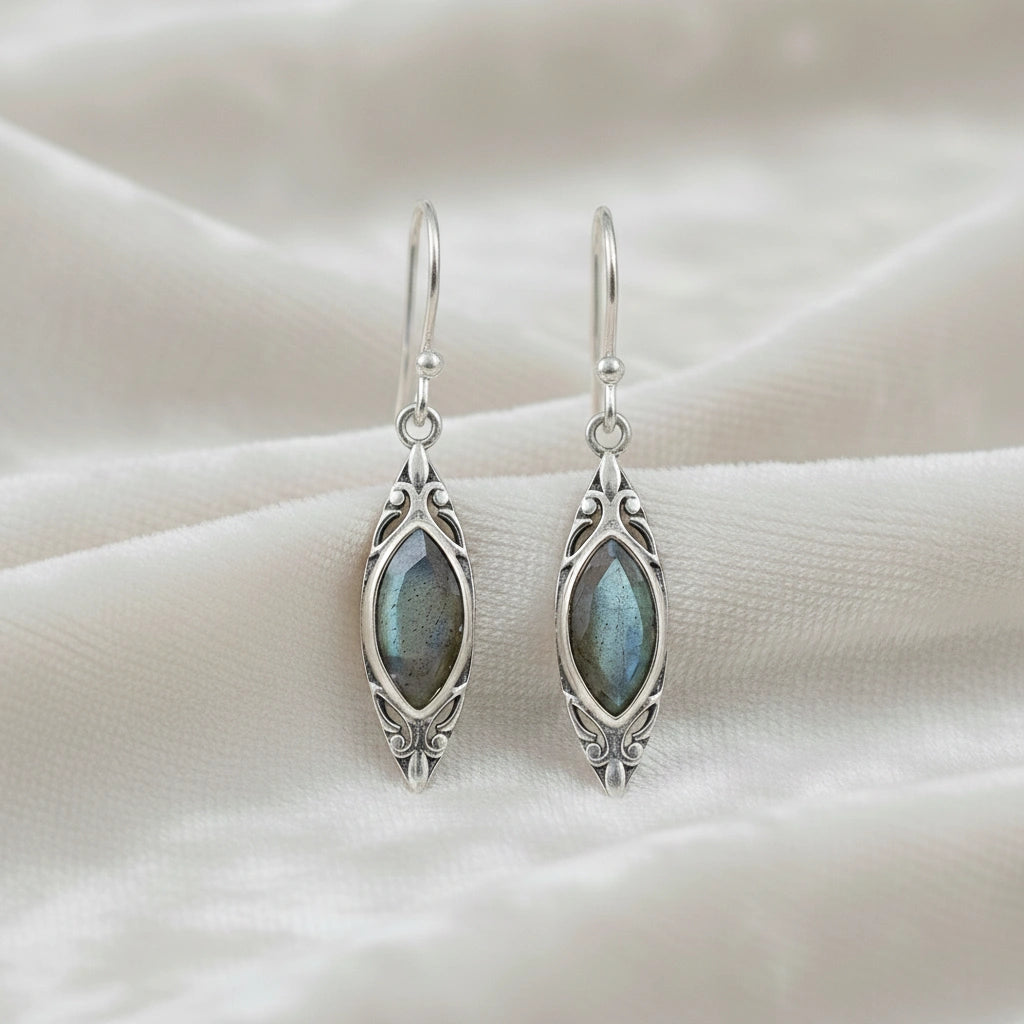 Marquise earrings silver dangle design with carved setting and central labradorite viewed straight on soft white fabric