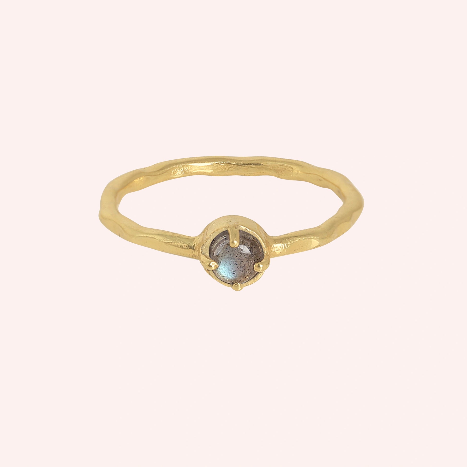 Minimalist ring featuring a round labradorite stone in a gold prong setting with a light pink background and straight on angle
