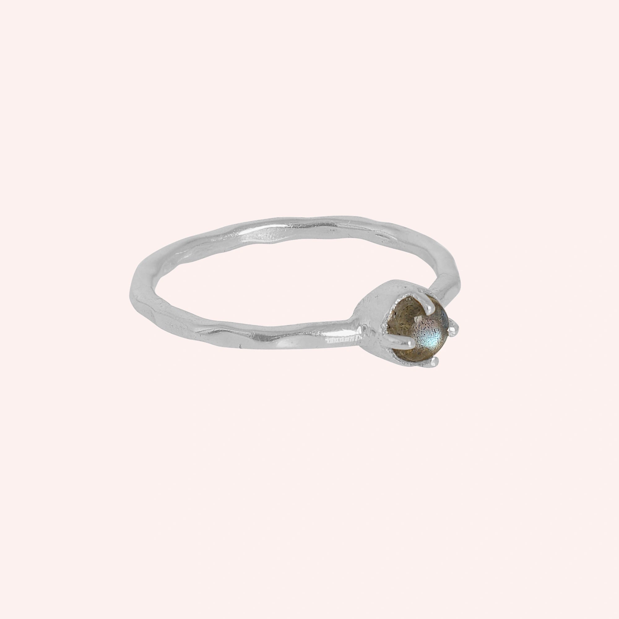 Minimalist ring featuring a small round labradorite stone in a silver setting on a light pink background at a slight right angle