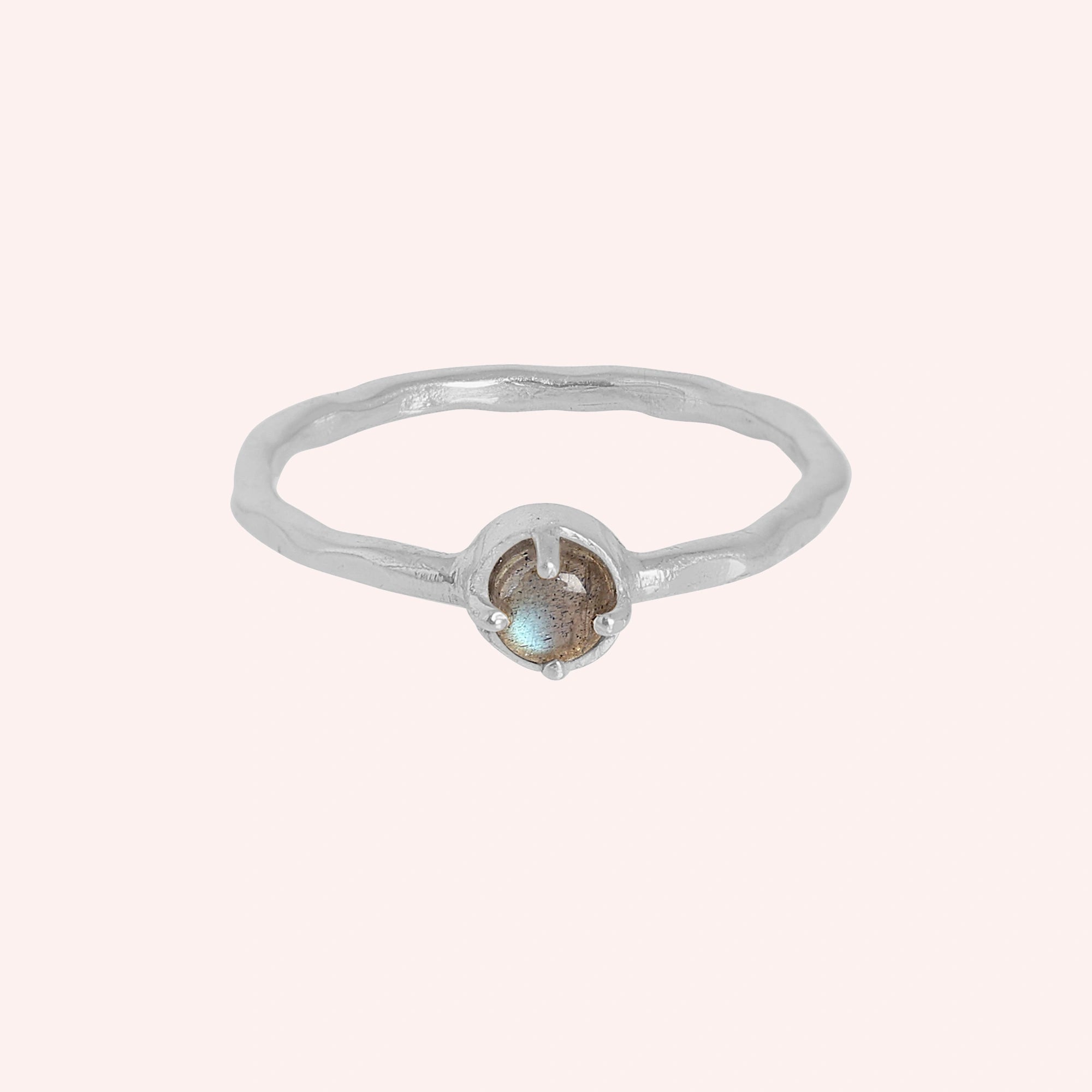 Minimalist ring featuring a round labradorite stone in a silver prong setting on a light pink background straight angle