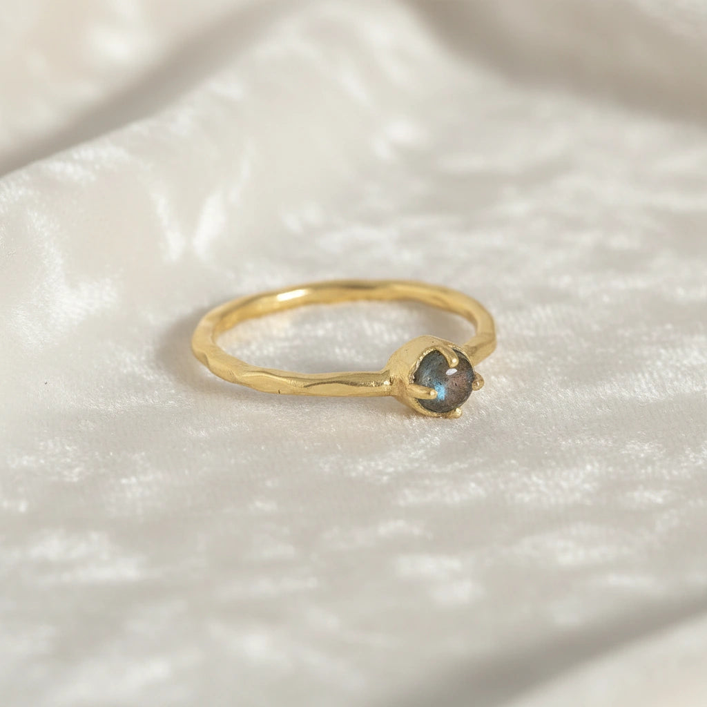 Minimalist ring featuring a round labradorite stone in a gold setting on a soft textured white fabric angled view