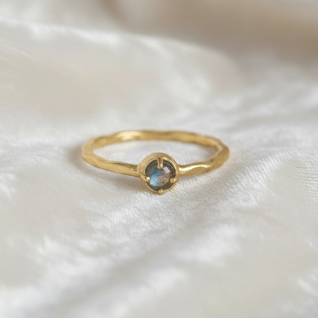 Minimalist ring featuring a round labradorite stone in a gold setting on a soft textured white fabric straight-on angle