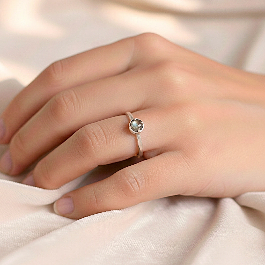 Minimalist ring featuring a round labradorite stone in a silver prong setting on a white fabric surface straight-on angle