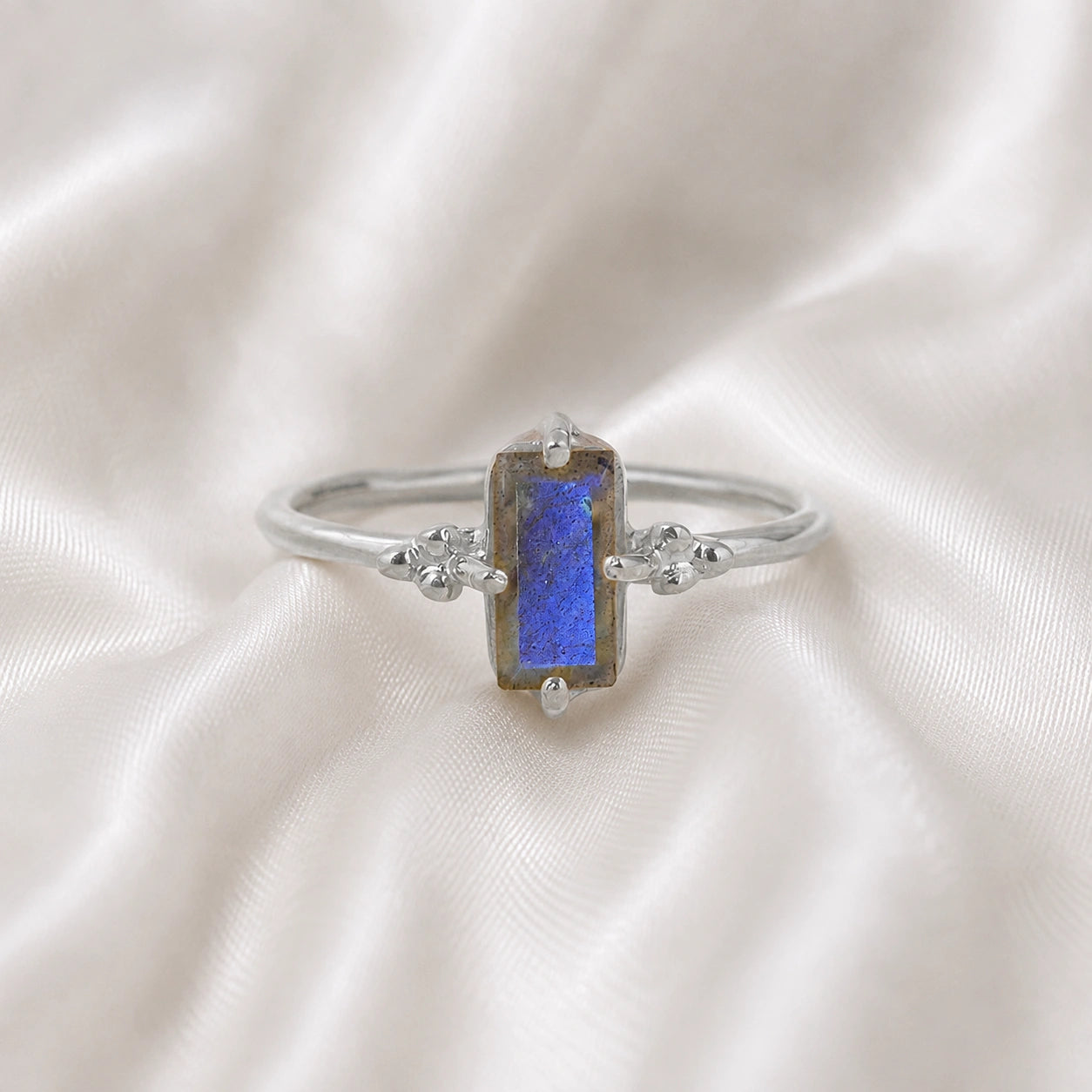 Labradorite_ring_with_baguette_shaped_labradorite_stone_in_sterling_silver_at_front_angle_view_on_soft_fabric_background