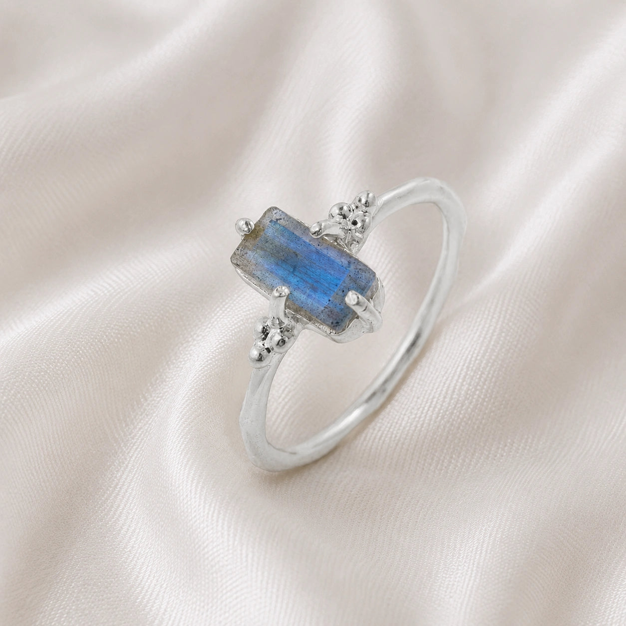 Labradorite_ring_with_baguette_shaped_labradorite_stone_in_sterling_silver_at_slight_angle_view_on_soft_fabric_background