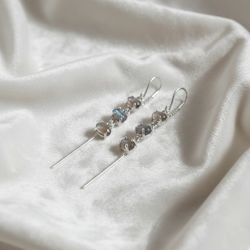 Threader earrings silver chain design with three linked labradorite stones viewed slightly angled on soft white fabric
