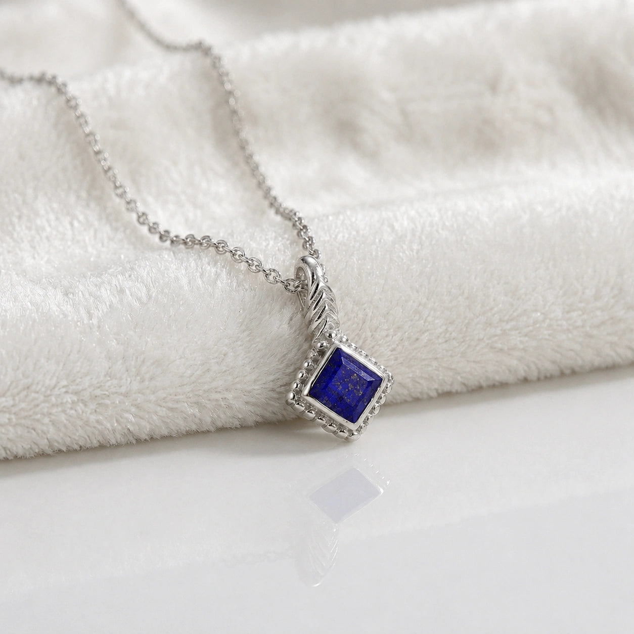 Birthstone_necklace_in_sterling_silver_with_square_cut_lapis_lazuli_pendant_in_slightly_angled_view_on_soft_white_fabric_background