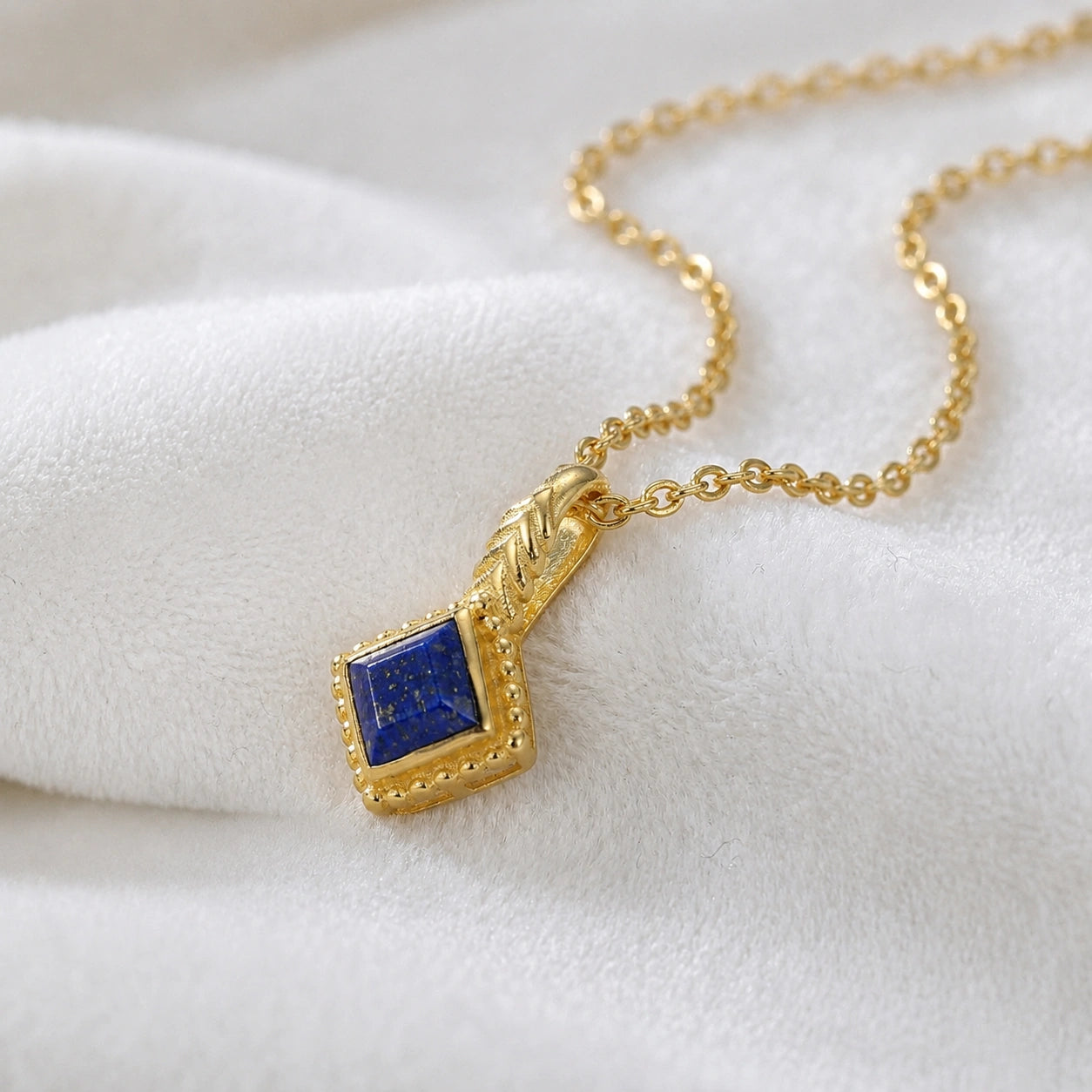 Birthstone_necklace_in_gold_plated_silver_with_square_cut_lapis_lazuli_pendant_in_slightly_angled_view_on_soft_white_fabric_background