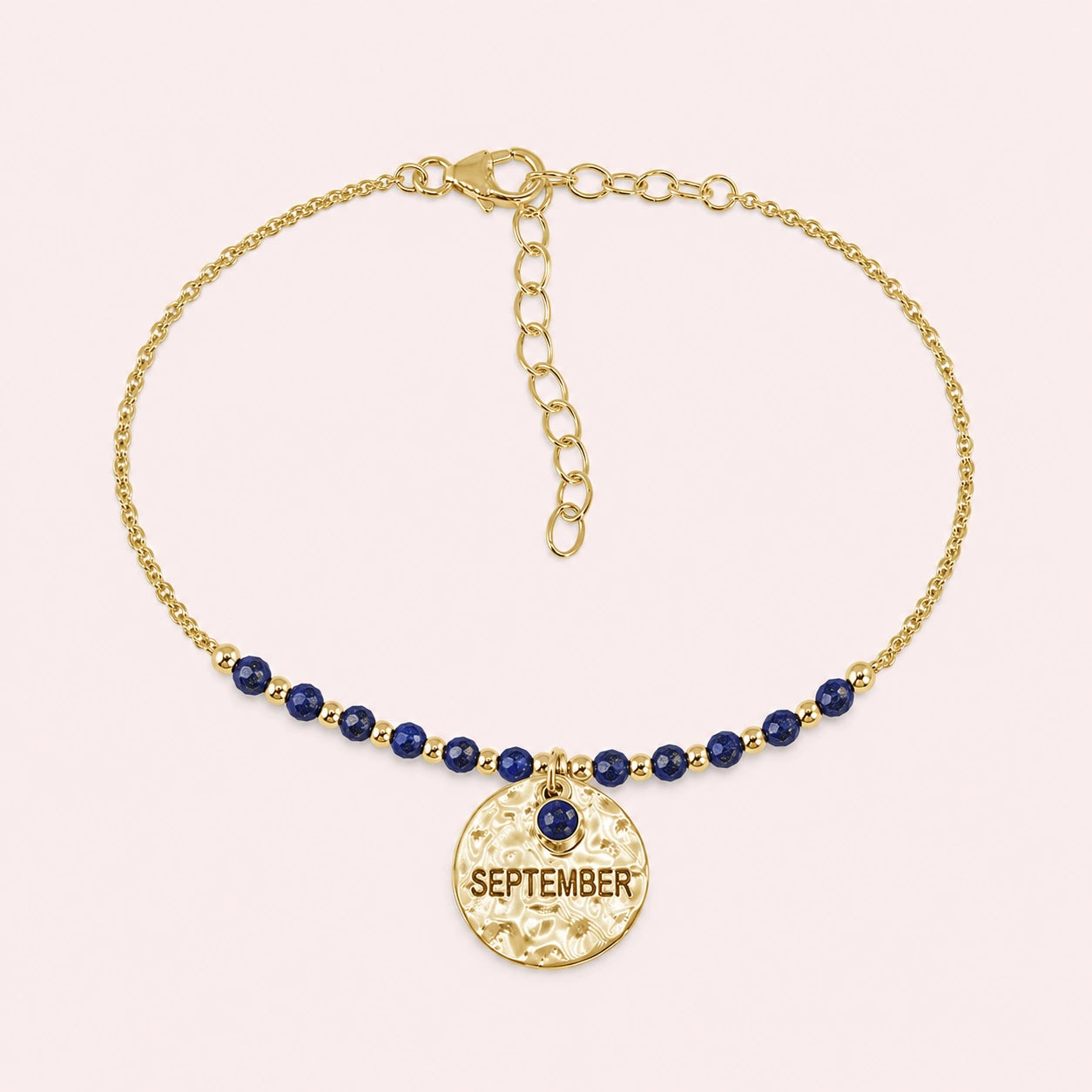 Birthstone_bracelet_in_gold_plated_silver_with_September_charm_and_lapis_lazuli_beads_on_fine_chain_on_solid_pink_background