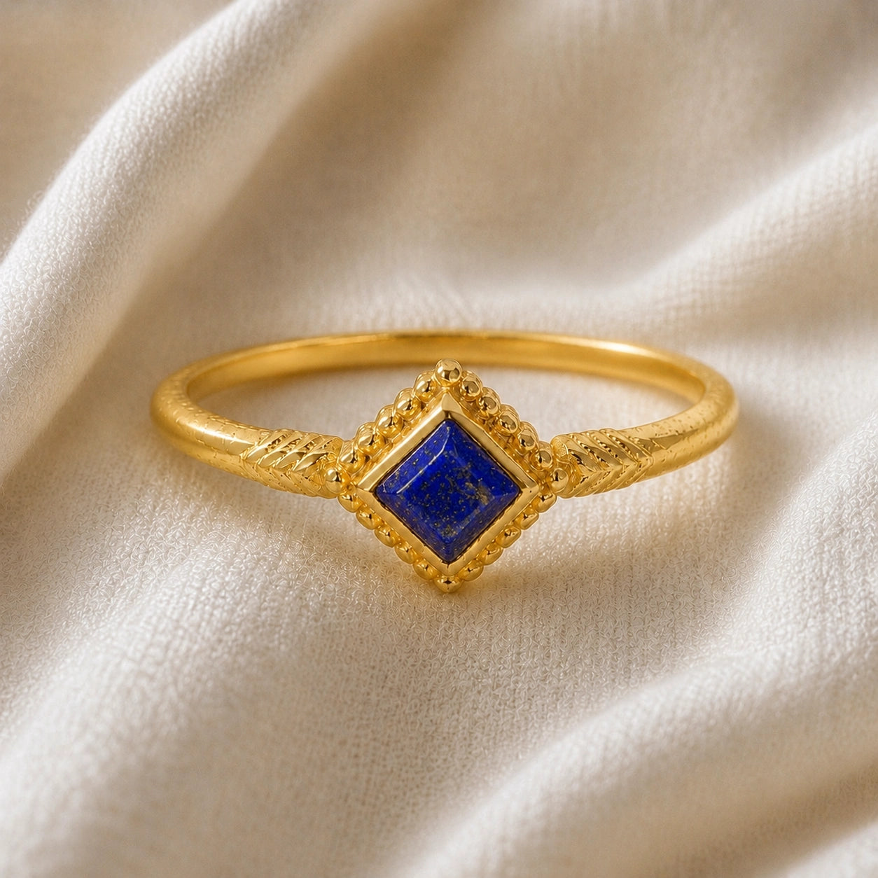 Princess_cut_ring_gold_plated_silver_with_square_lapis_lazuli_and_detailed_band_front_angle_view_on_soft_fabric_background