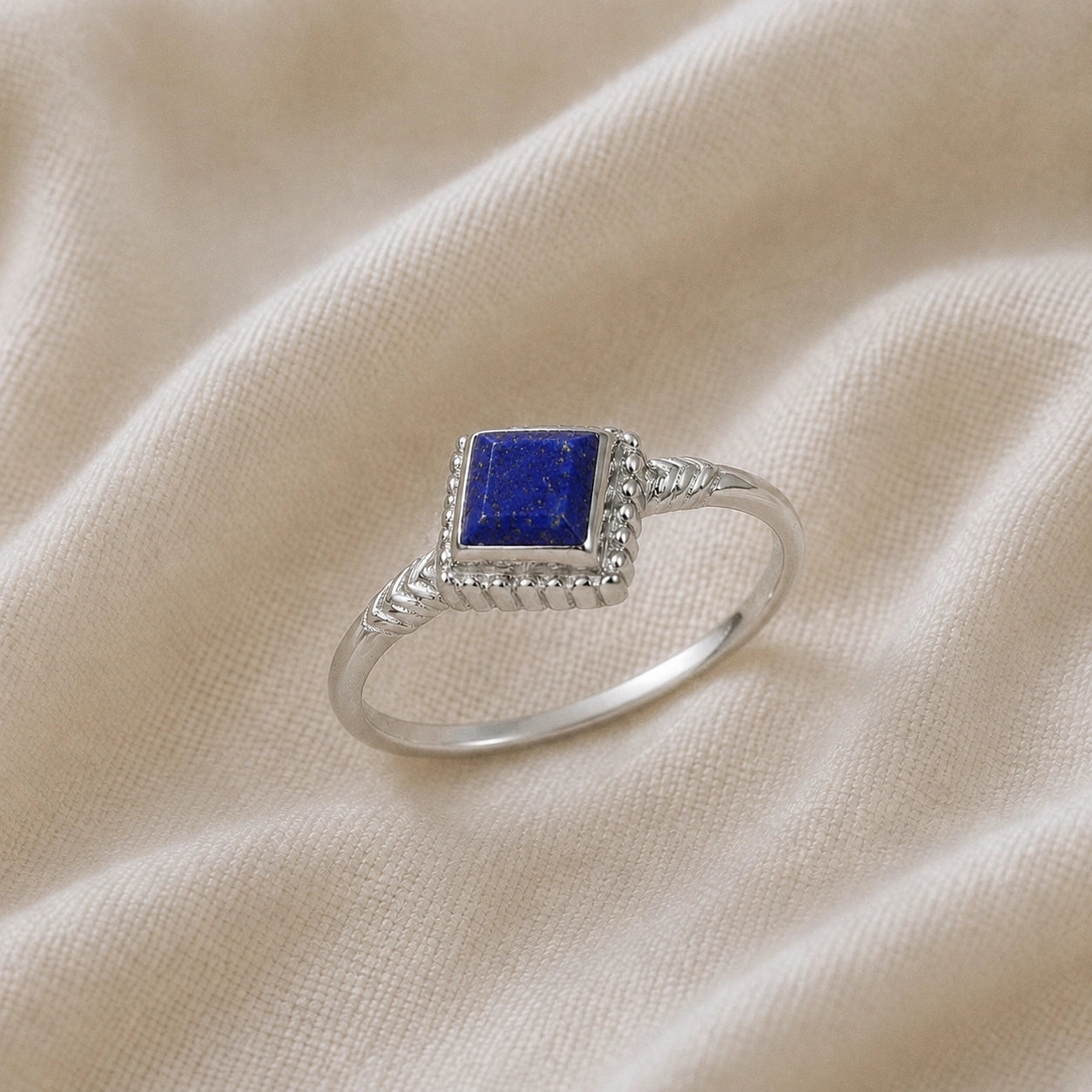 Princess_cut_ring_sterling_silver_with_square_lapis_lazuli_and_detailed_band_slightly_tilted_view_on_soft_fabric_background