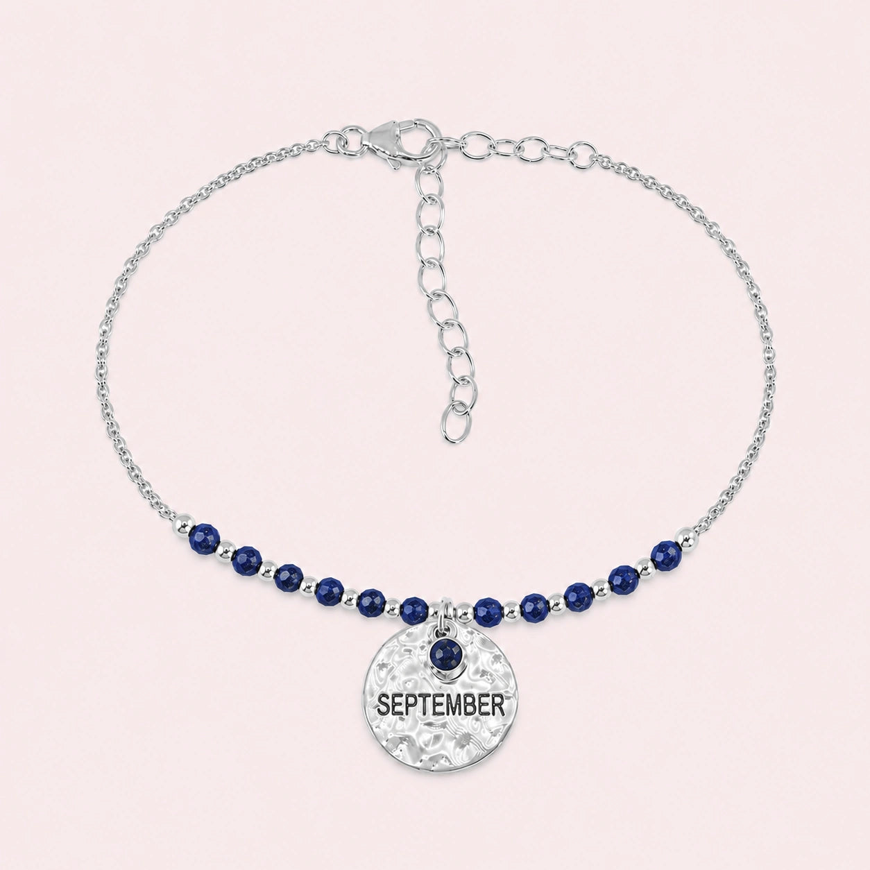 Birthstone_bracelet_in_sterling_silver_with_September_charm_and_lapis_lazuli_beads_on_fine_chain_on_solid_pink_background