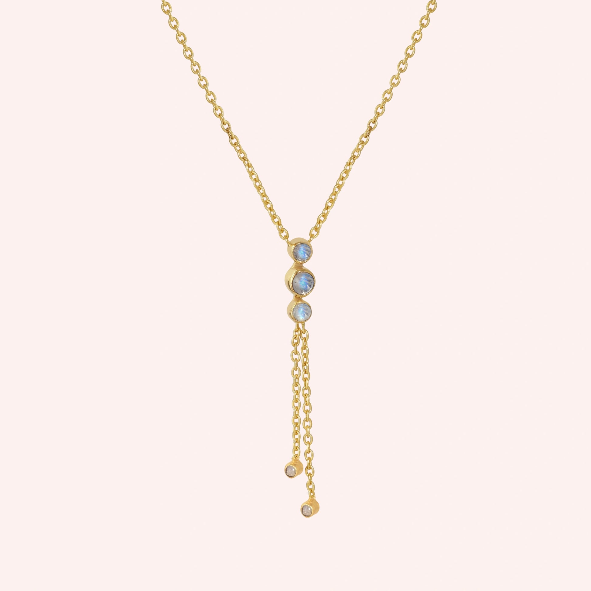 Lariat_necklace_in_gold_plated_silver_at_slight_angle_featuring_moonstone_drops_on_solid_pink_background