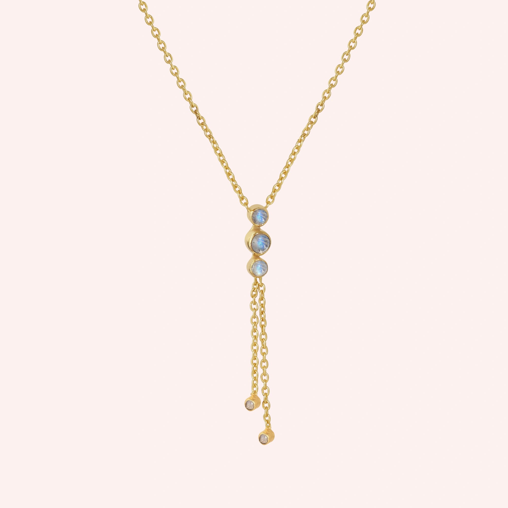 Lariat_necklace_in_gold_plated_silver_at_slight_angle_featuring_moonstone_drops_on_solid_pink_background