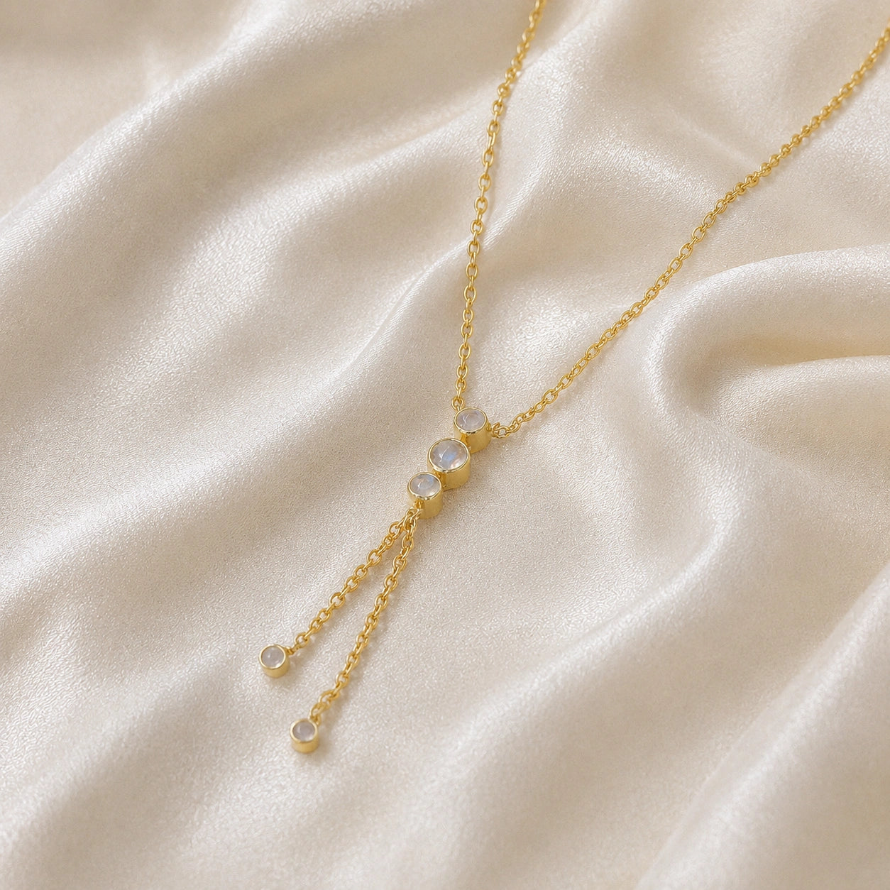 Lariat_necklace_in_gold_plated_silver_at_slight_angle_featuring_moonstone_drops_on_soft_fabric_background