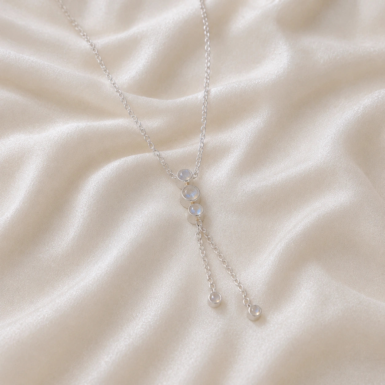Lariat_necklace_in_sterling_silver_at_slight_angle_featuring_moonstone_drops_on_soft_fabric_background