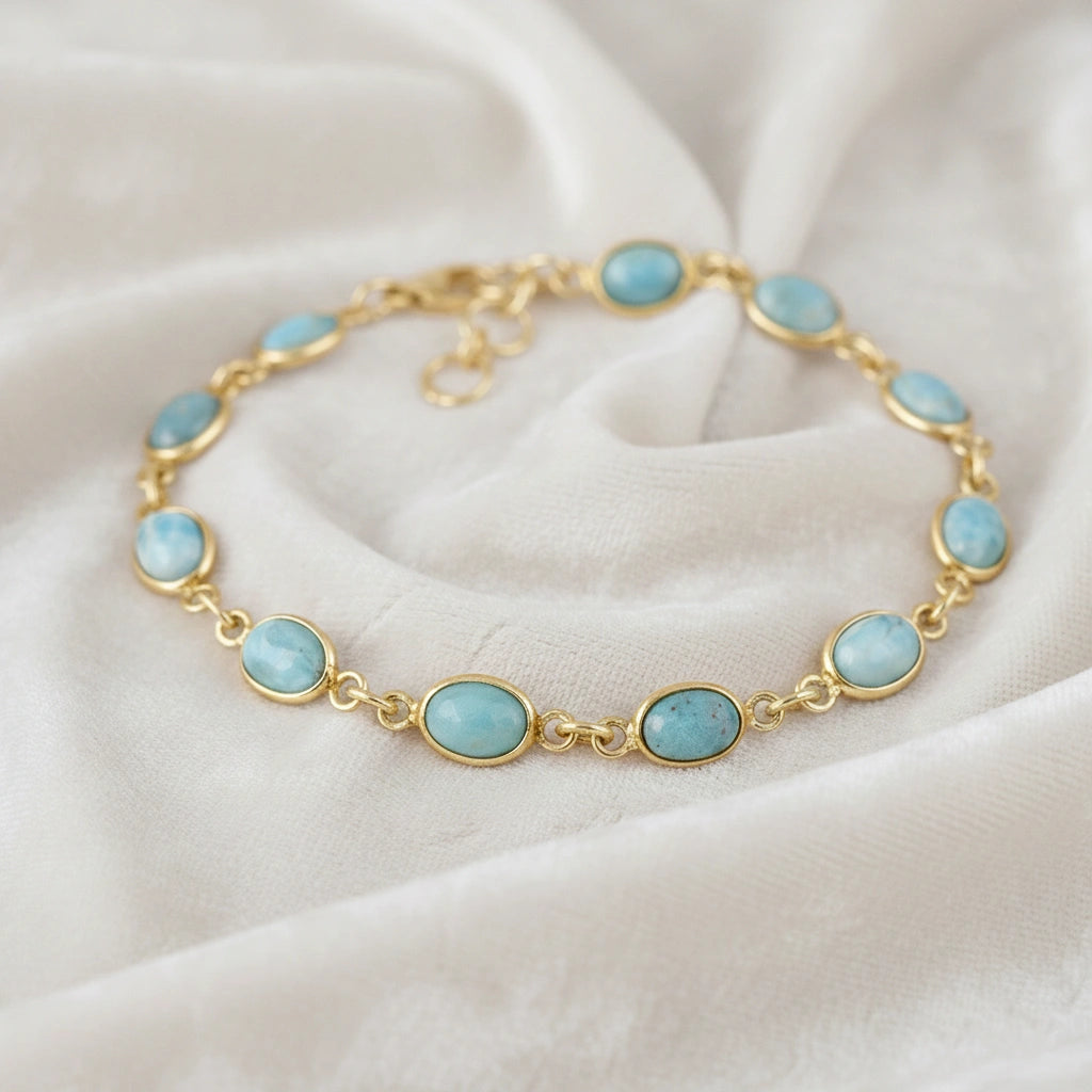 Gold plated larimar bracelet with oval links gemstone chain on an off white velvet fabric from a straight angle view