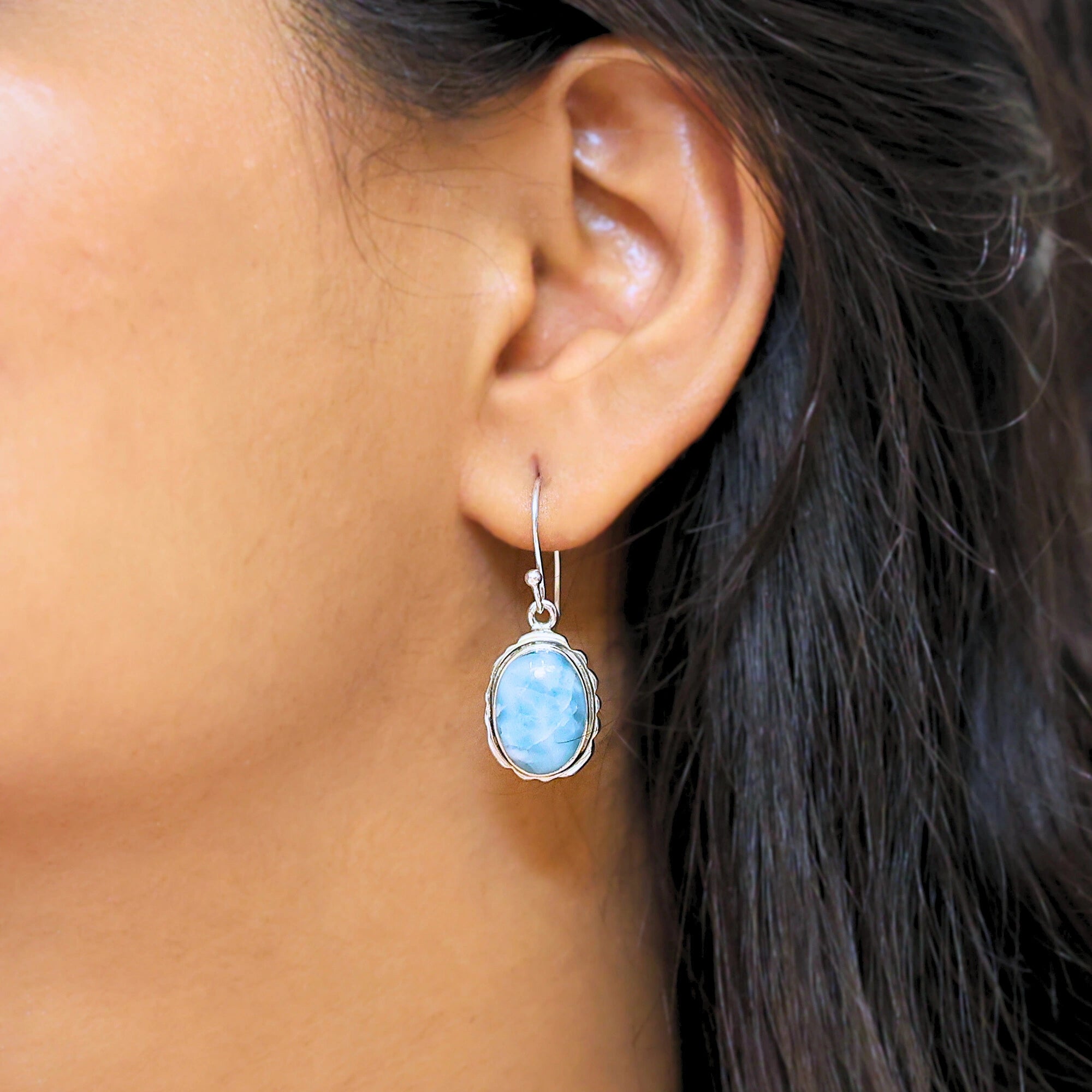 Silver dangling earring blue Larimar oval stone set in a serrated bezel worn on a model ear side view profile angle