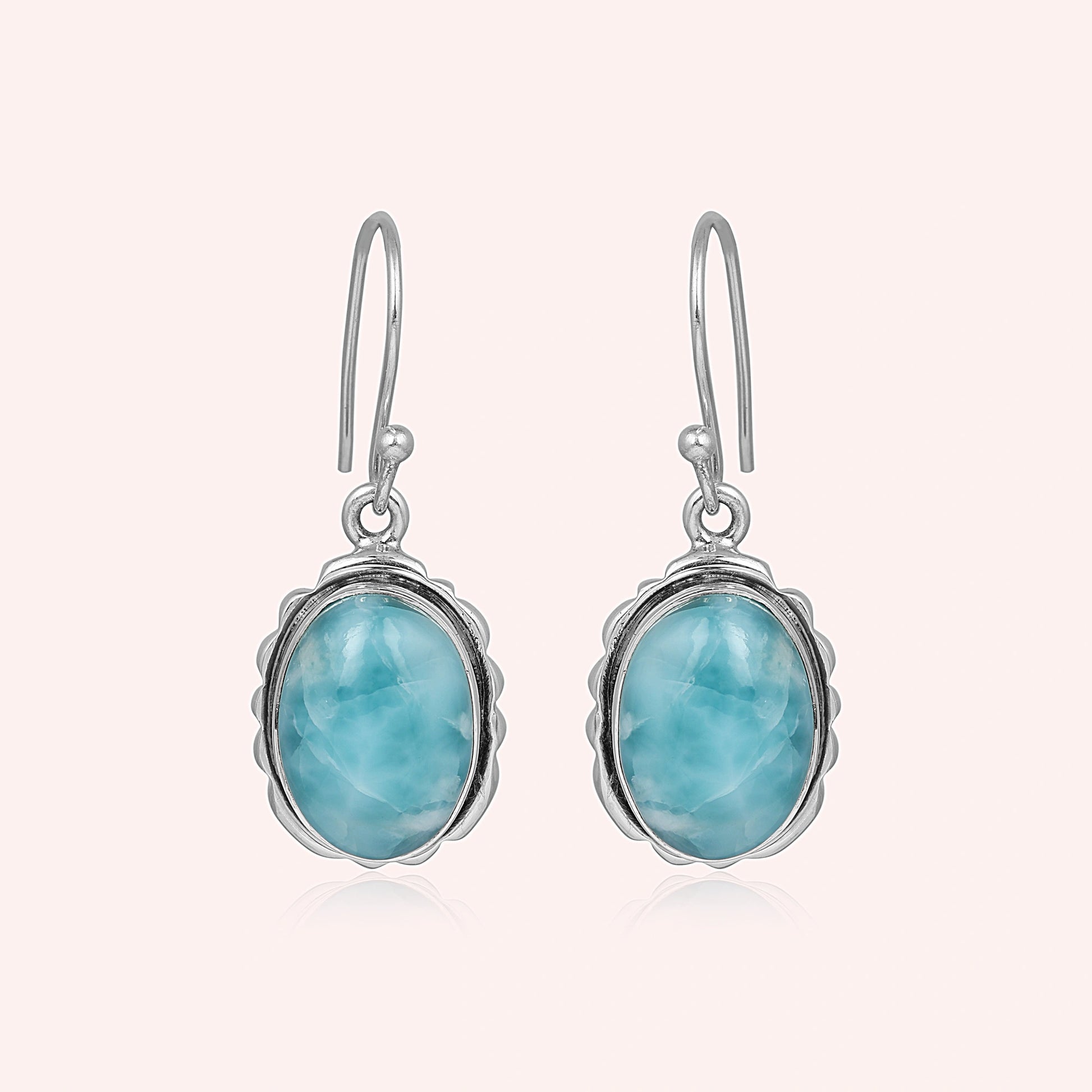Silver dangling earring blue larimar oval stone set in decorative bezel a delicate side angle on soft light pink background
