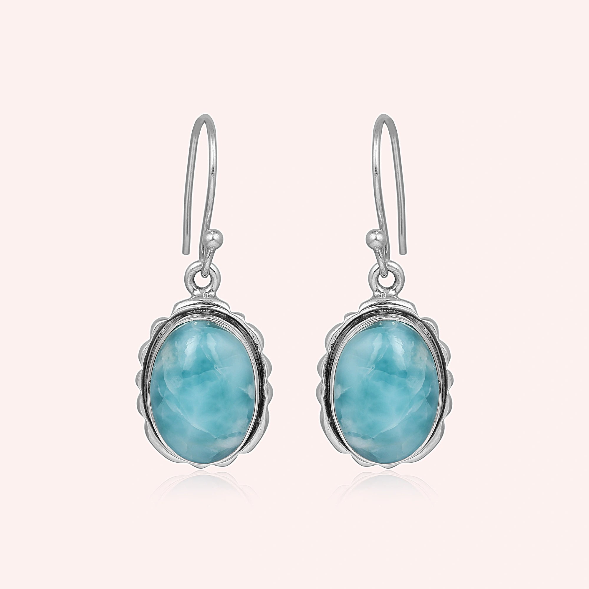 Silver dangling earring blue larimar oval stone set in decorative bezel a delicate side angle on soft light pink background