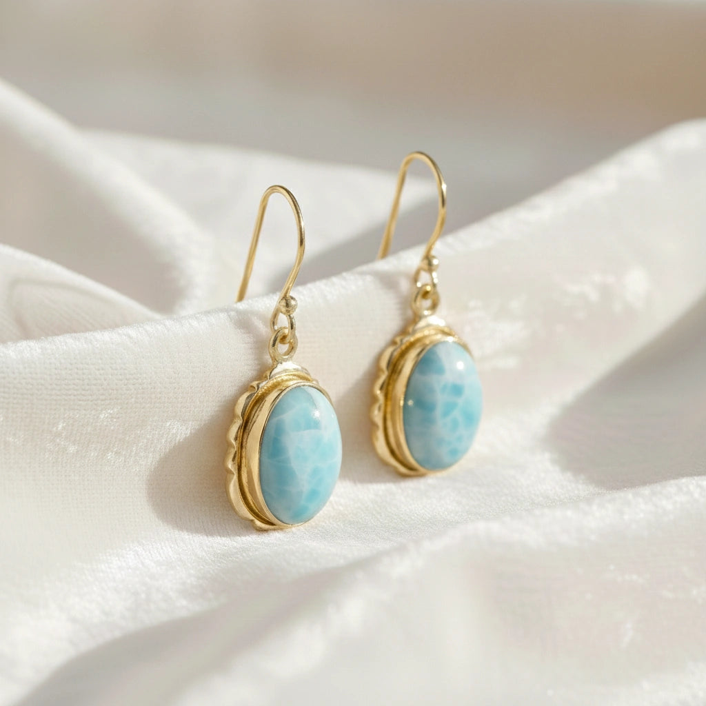 Silver dangling earring with cushion cut larimar gemstones with gold plating on white draped fabric from an angled view