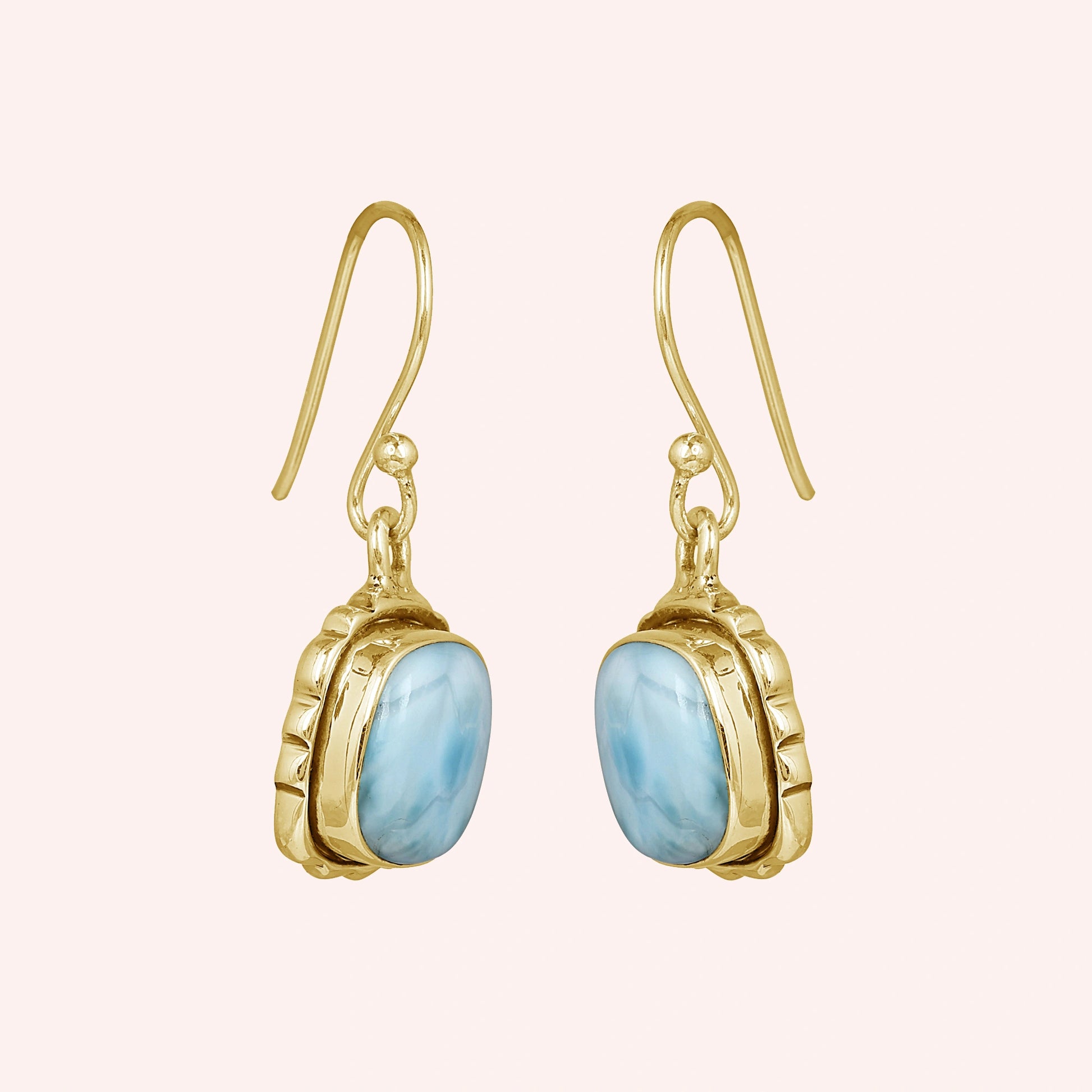 Gold plated sterling silver dangle earrings with cushion-cut larimar stones in a side angle on a plain pink background
