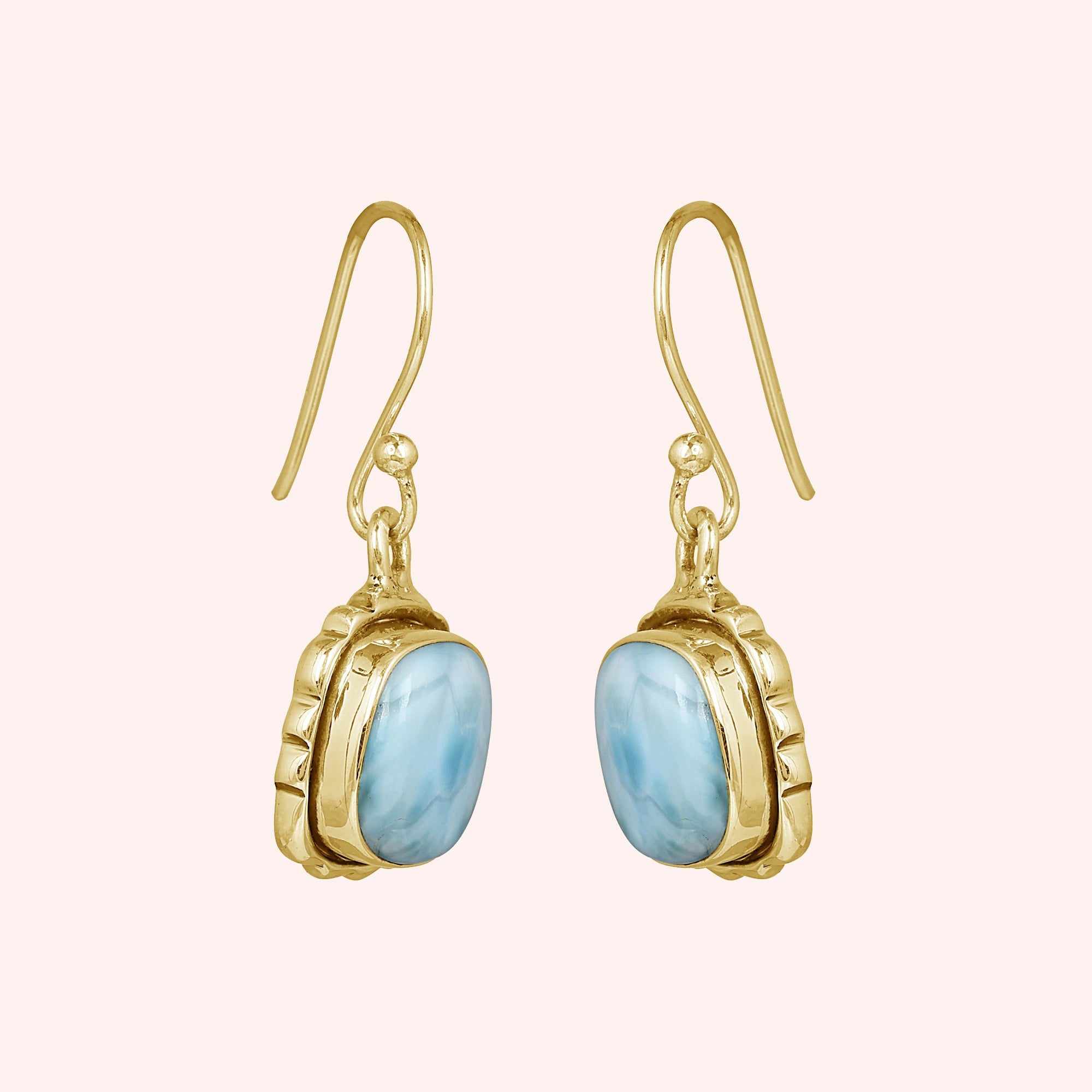 Gold plated sterling silver dangle earrings with cushion-cut larimar stones in a side angle on a plain pink background