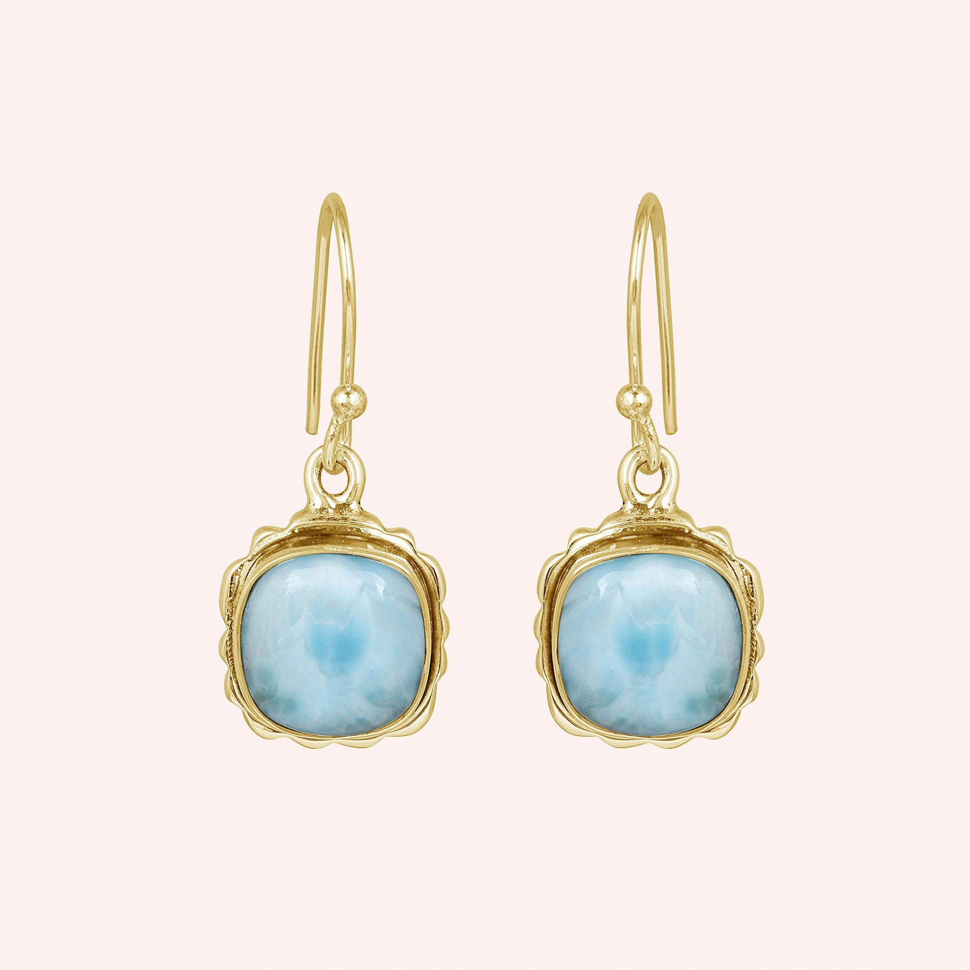 Gold plated sterling silver dangle earrings with cushion-cut larimar stones in a face-on view on a plain pink background