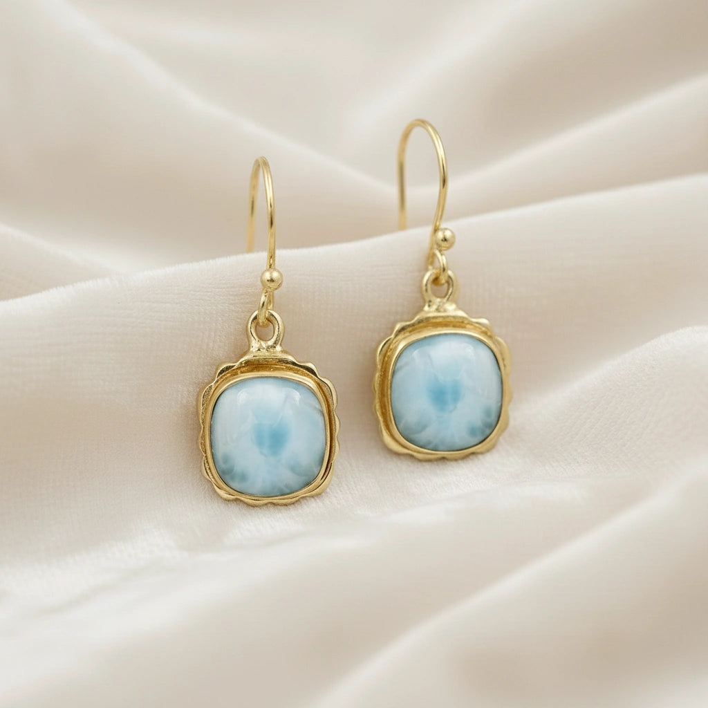 Gold plated sterling silver dangle earrings with cushion cut larimar gemstones on white draped fabric from a straight angle view