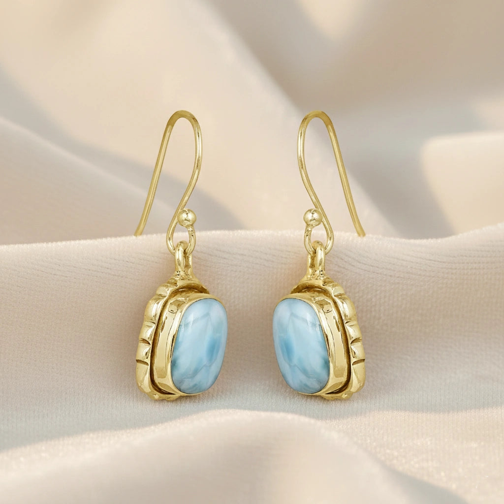 Gold plated sterling silver dangle earrings with a cushion cut gemstone on an off white draped fabric from a slightly angled view