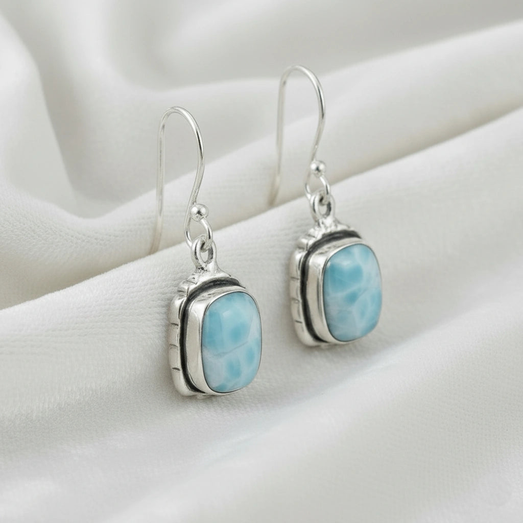 Sterling silver dangle earrings with cushion cut larimar gemstones on white draped fabric from a slightly angled view
