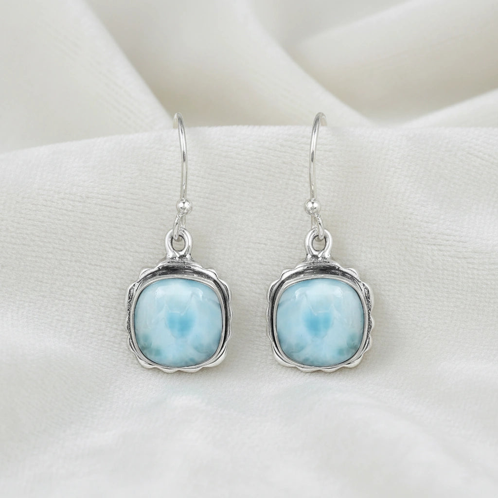 Sterling silver dangle earrings with cushion cut larimar stones on white draped fabric from a straight angle view