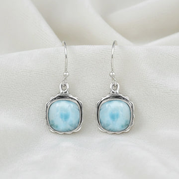 Sterling silver dangle earrings with cushion cut larimar stones on white draped fabric from a straight angle view