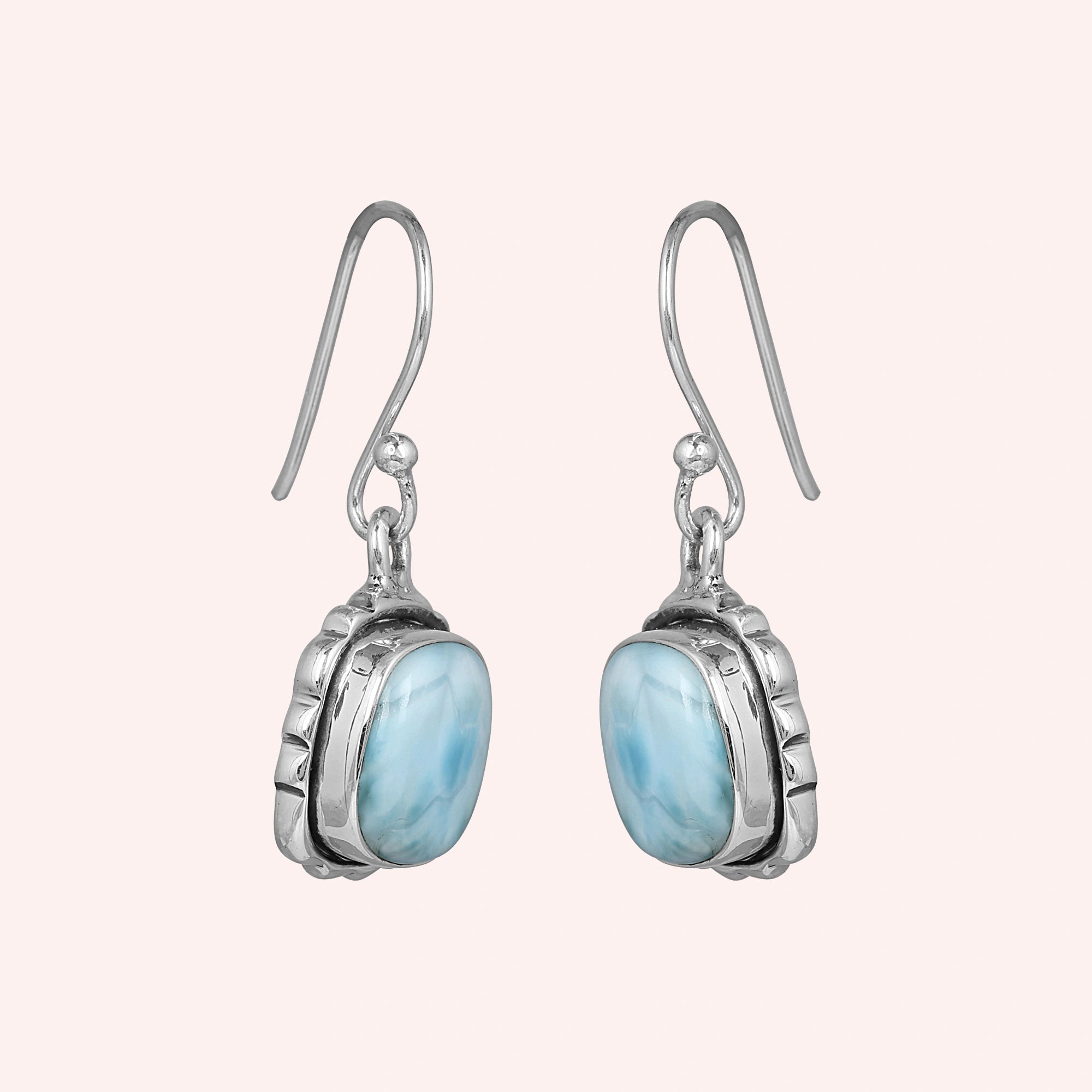 Sterling silver dangle earrings with cushion-cut larimar stones in a side angle on a minimal pink background