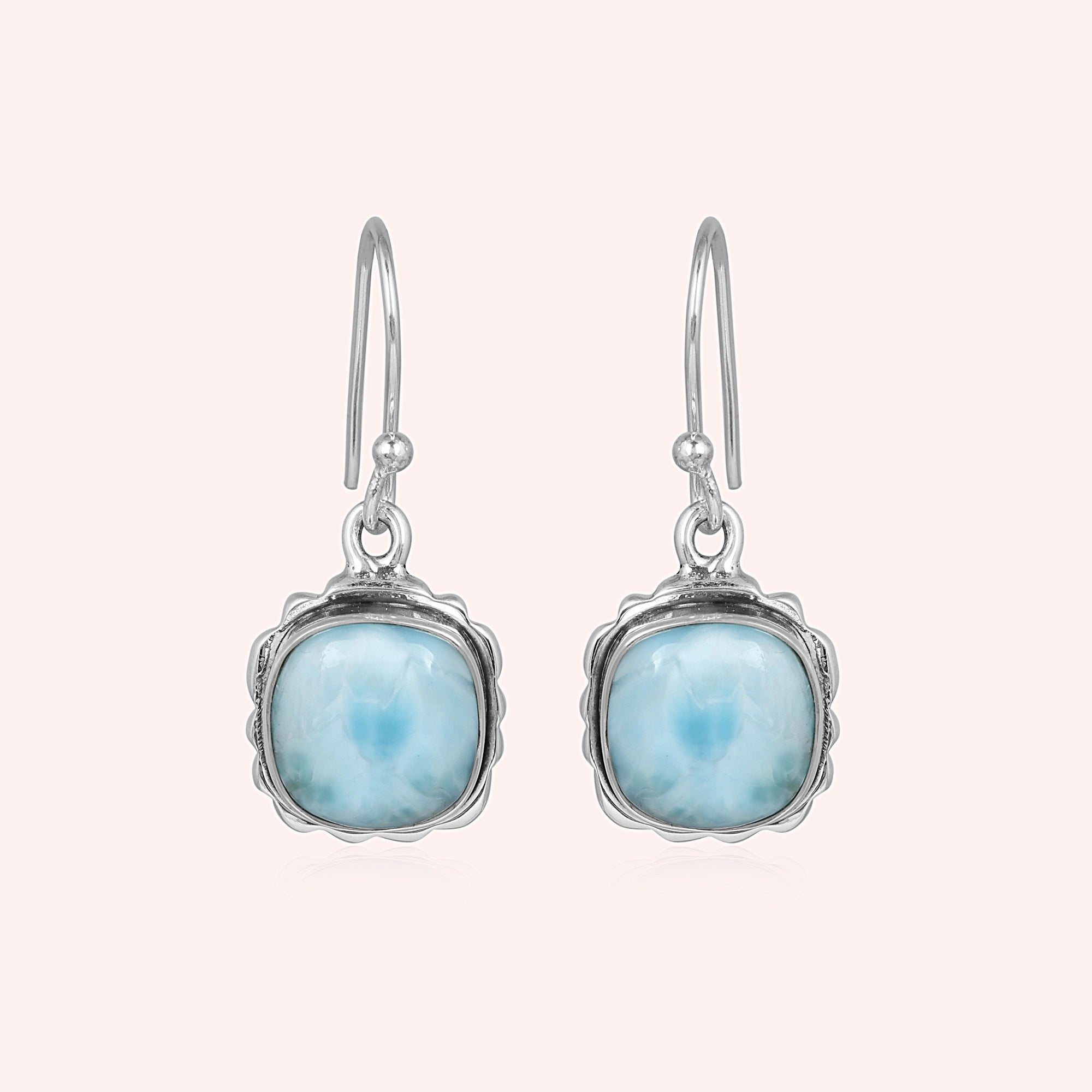 Sterling silver dangle earrings with cushion-cut larimar stones on a plain pink background shot at a straight angle