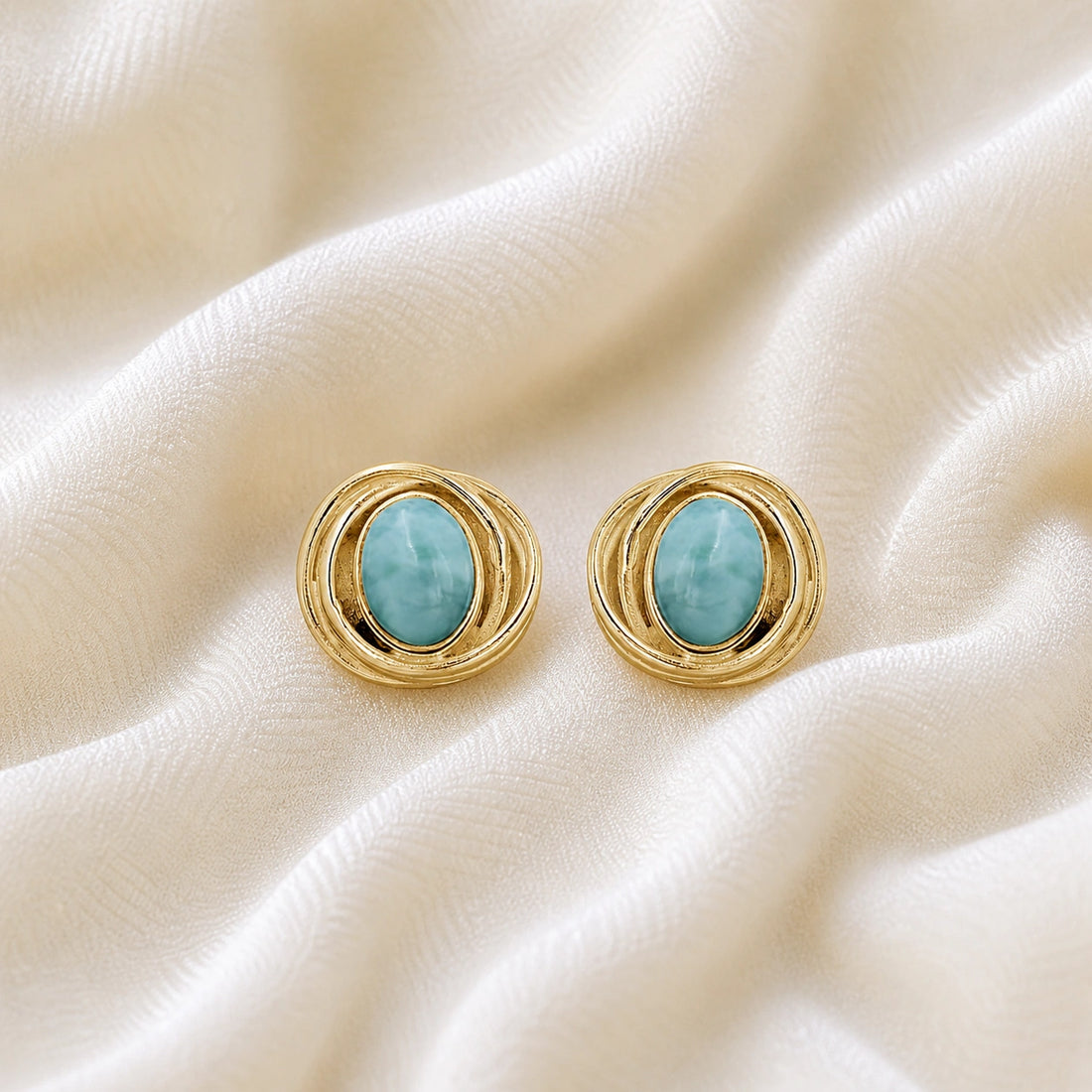 Larimar_earrings_gold_plated_silver_stud_design_with_oval_larimar_stone_shown_at_front_angle_on_soft_fabric_background