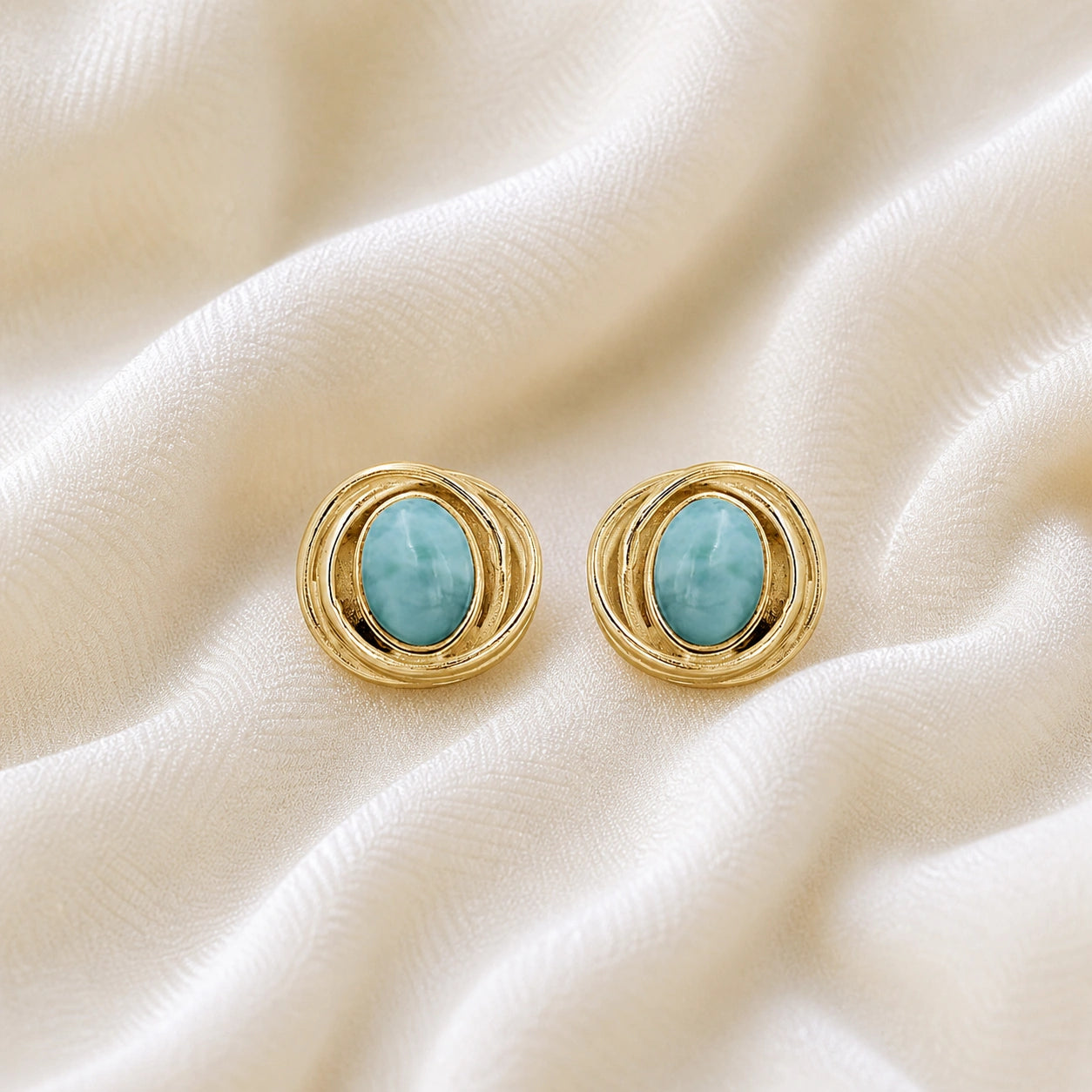 Larimar_earrings_gold_plated_silver_stud_design_with_oval_larimar_stone_shown_at_front_angle_on_soft_fabric_background
