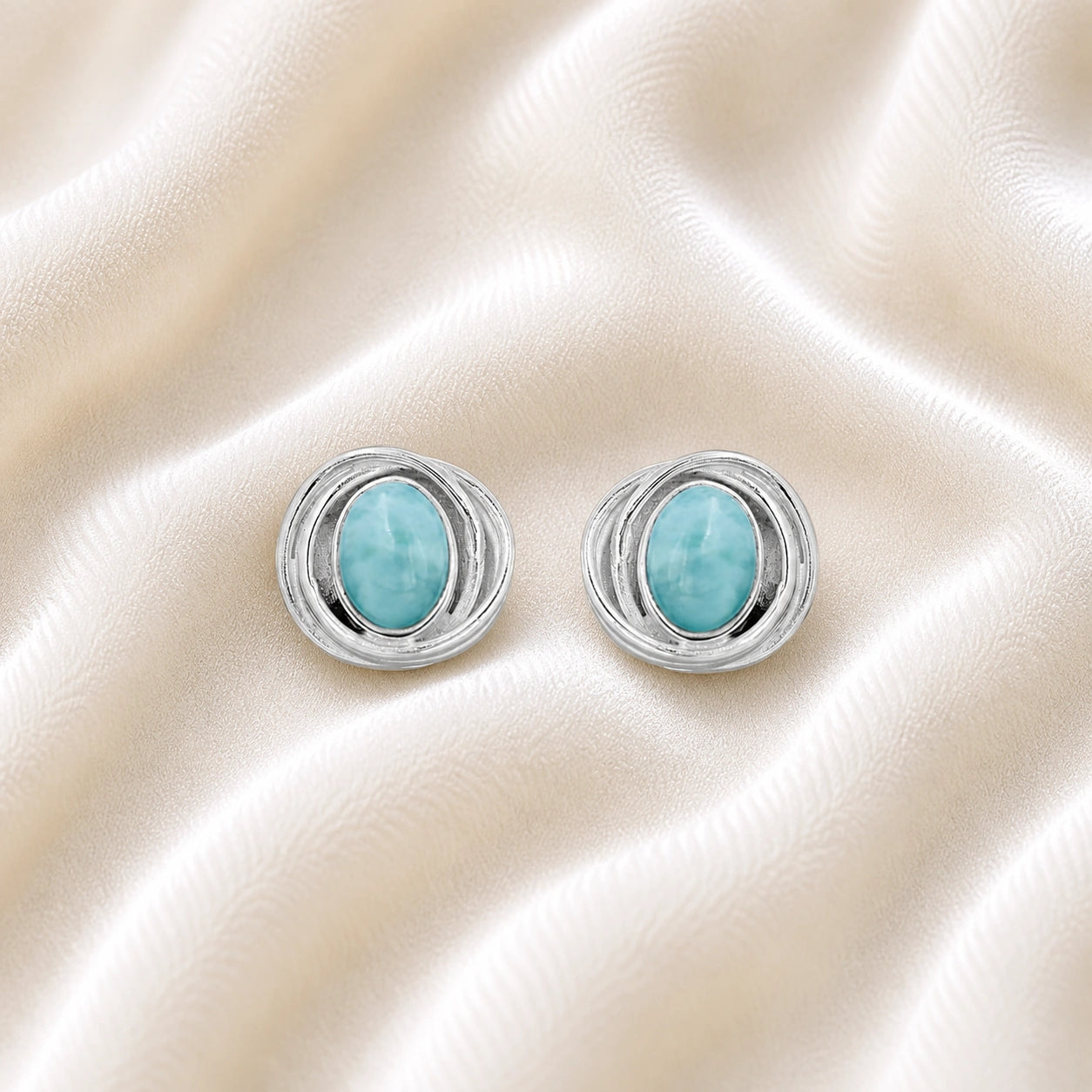Larimar_earrings_sterling_silver_stud_design_with_oval_larimar_stone_shown_at_front_angle_on_soft_fabric_background