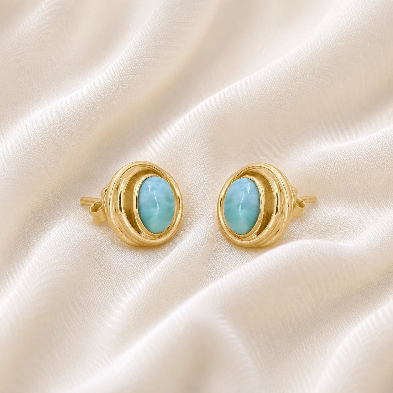 Larimar_earrings_gold_plated_silver_stud_design_with_oval_larimar_stone_shown_slightly_angled_on_soft_fabric_background
